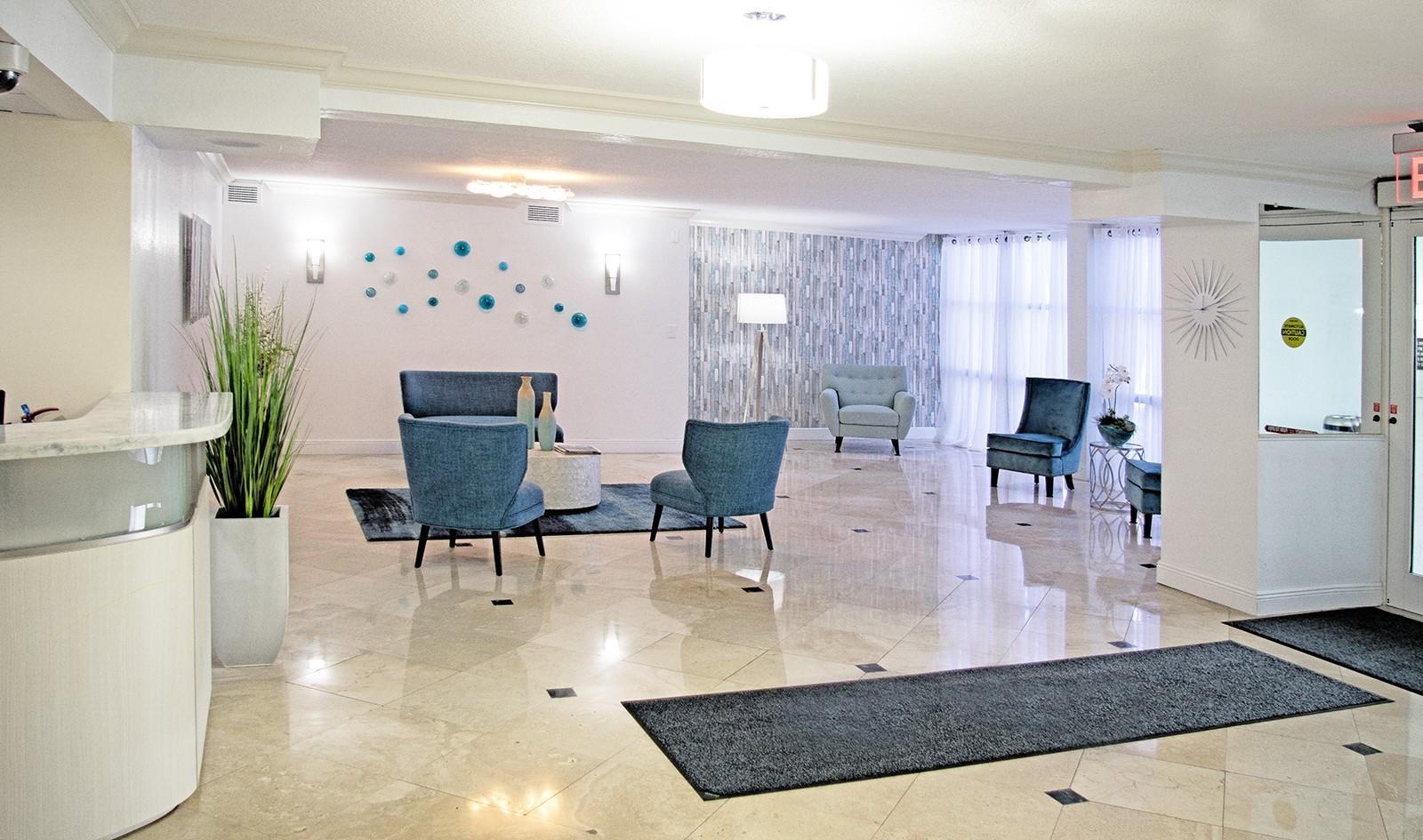 A modern lobby features blue armchairs, a sofa, tiled floors, and decorative wall art — 800 Parkview Drive # 411, Hallandale Beach FL 33009, HALLANDALE BEACH, FL