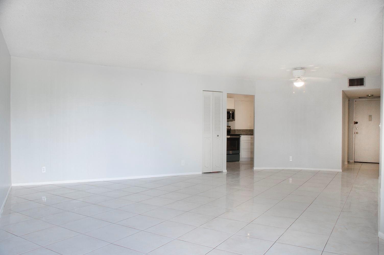 An empty room with white walls, white tile flooring, a ceiling fan, and a kitchen doorway — 800 Parkview Drive # 411, Hallandale Beach FL 33009, HALLANDALE BEACH, FL