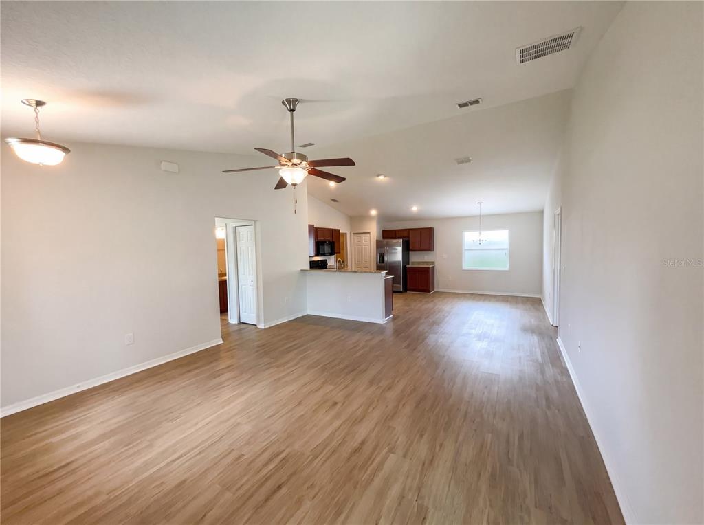 An open-concept living area features light wood-look flooring, a ceiling fan, and a kitchen — 2005 ORANGE AVENUE, ST CLOUD, FL