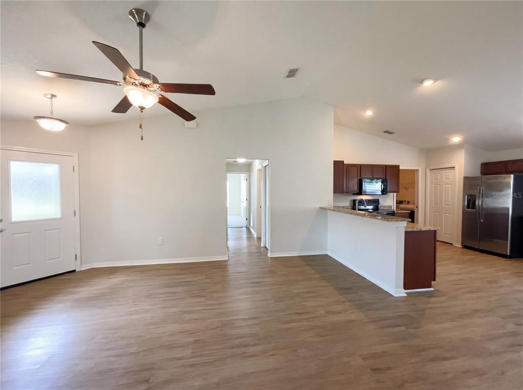 A living room with wood-look flooring opens to a kitchen with dark cabinets and appliances — 2005 ORANGE AVENUE, ST CLOUD, FL