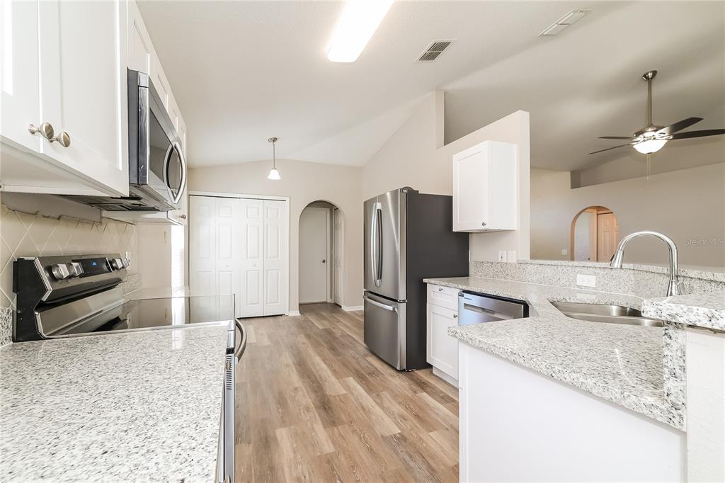 A kitchen features white cabinets, granite countertops, stainless steel appliances, and wood-look flooring — 416 ELGIN BOULEVARD, DAVENPORT, FL