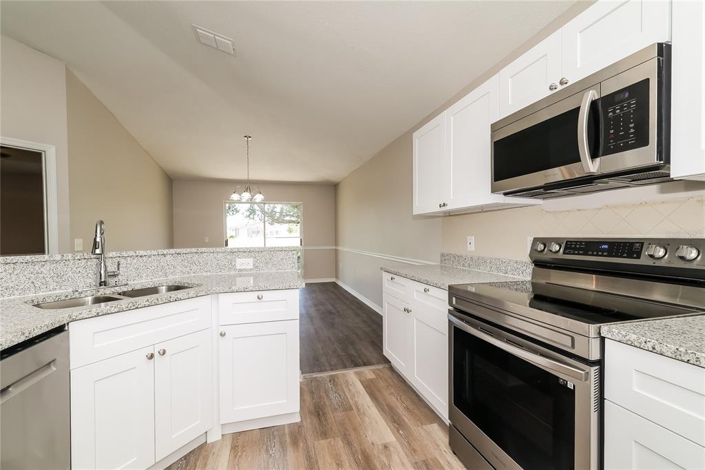 A kitchen with white cabinets, granite countertops, and stainless steel appliances opens to a dining area — 416 ELGIN BOULEVARD, DAVENPORT, FL