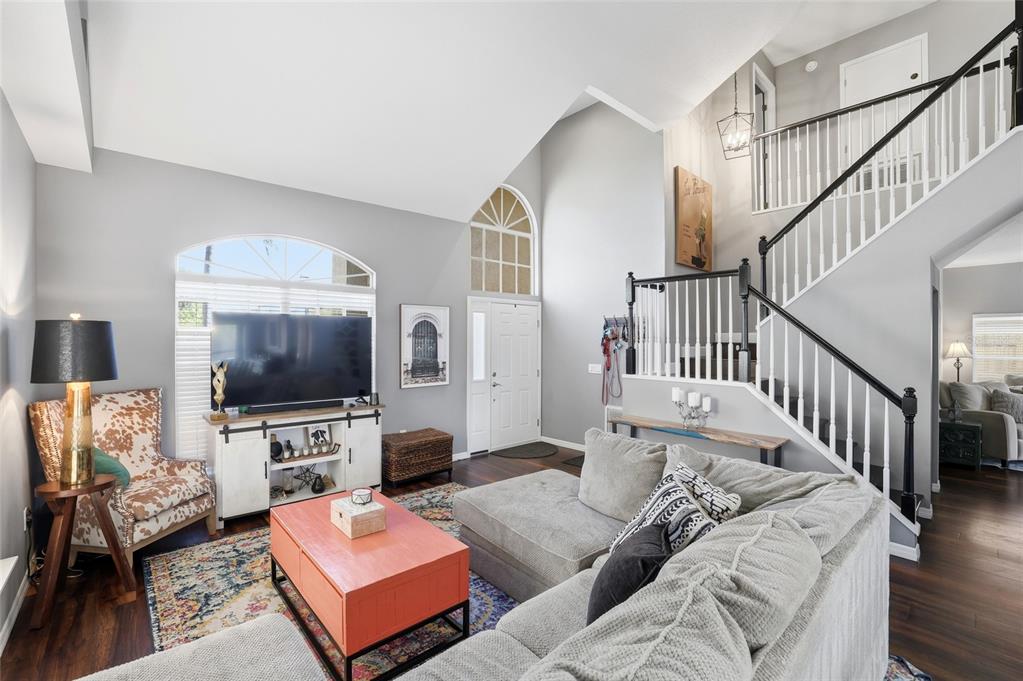 A living room features a vaulted ceiling, a staircase with black railings, and hardwood floors — 11235 CLAYRIDGE DRIVE, TAMPA, FL