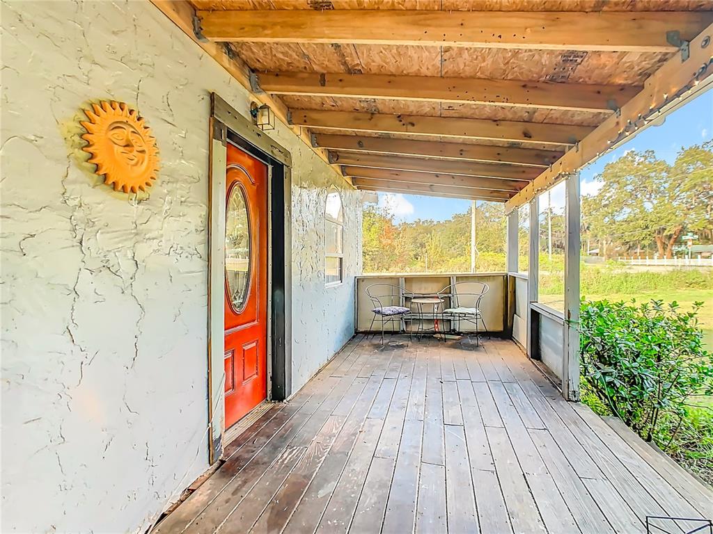 A covered wooden porch features a red front door, a sun wall decoration, and seating — 900 N 30TH STREET, HAINES CITY, FL