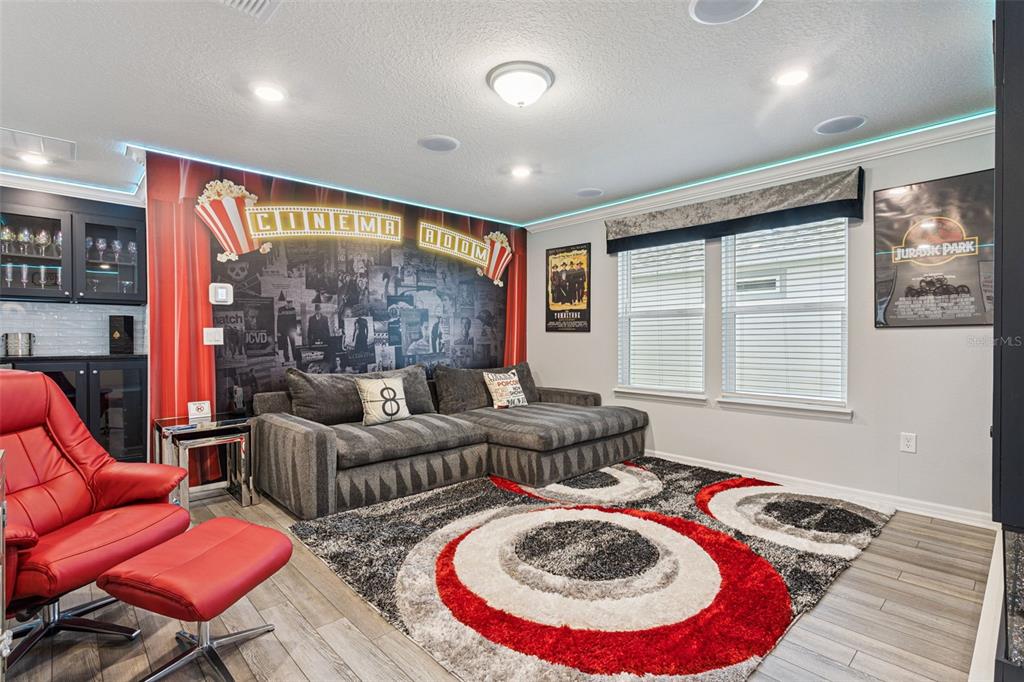 A home theater room features a sectional sofa, red recliner, and cinema-themed wall mural — 16205 SAINT KITTS CIRCLE, CLERMONT, FL
