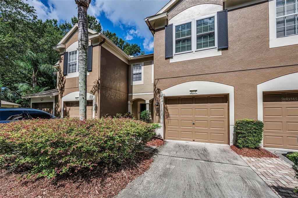A two-story townhouse exterior features a tan stucco facade, a garage, and a driveway — 8414 SANDY BEACH STREET, TAMPA, FL
