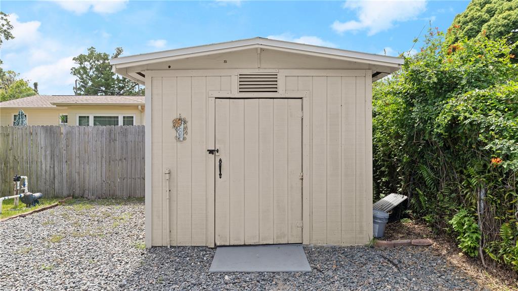 A beige wooden storage shed stands on a gravel yard in front of a fence — 358 S ORCHARD STREET, ORMOND BEACH, FL