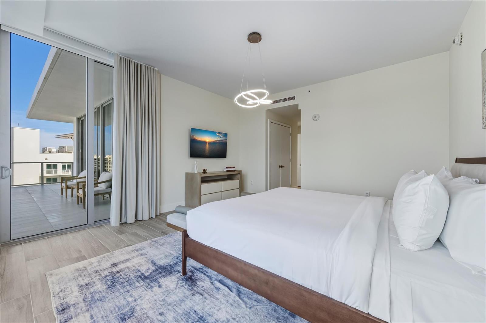 A modern bedroom features a bed, a television, a light fixture, and a balcony entrance — 3100 N Ocean Drive # P1802, Riviera Beach FL 33404, RIVIERA BEACH, FL