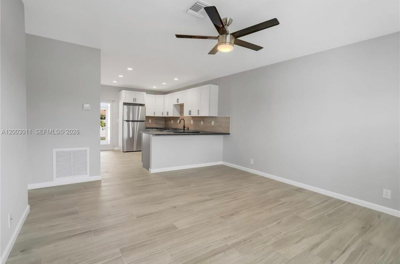 An open-concept kitchen with white cabinets and stainless steel appliances overlooks a living area — 2550 N Dixie Hwy # 2570, Boca Raton FL 33431, BOCA RATON, FL
