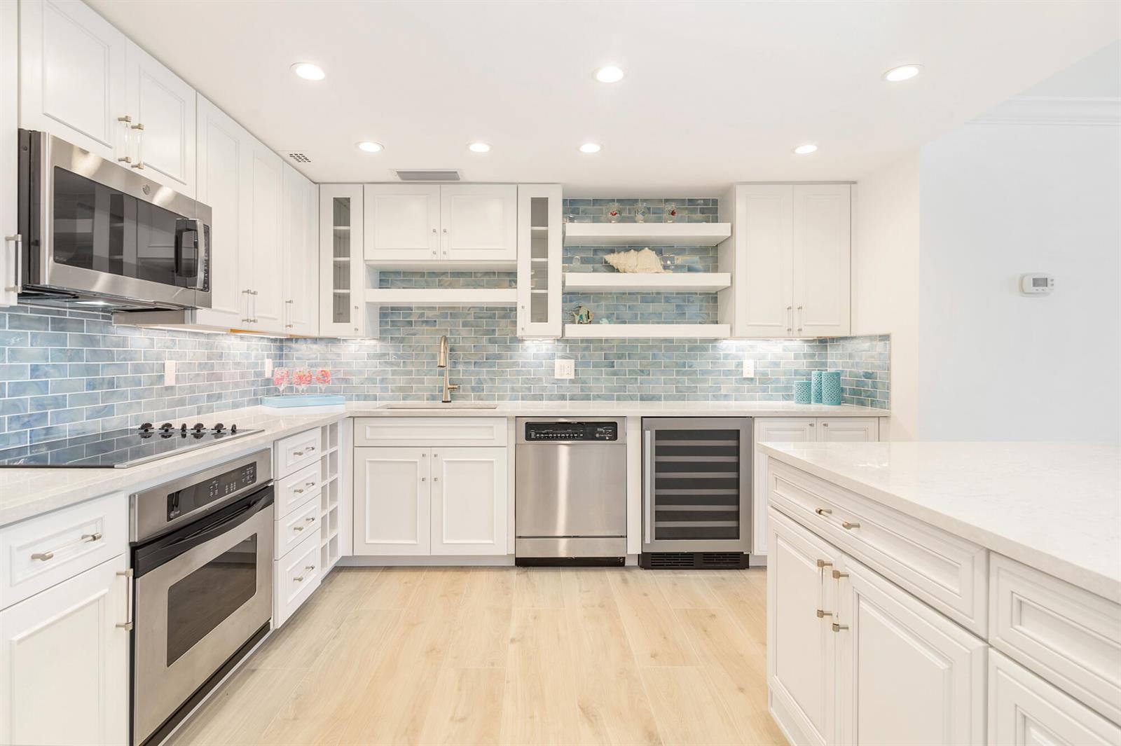 A modern white kitchen features blue subway tile backsplashes, stainless steel appliances, and light flooring — 354 Chilean Avenue # 6c, Palm Beach FL 33480, PALM BEACH, FL