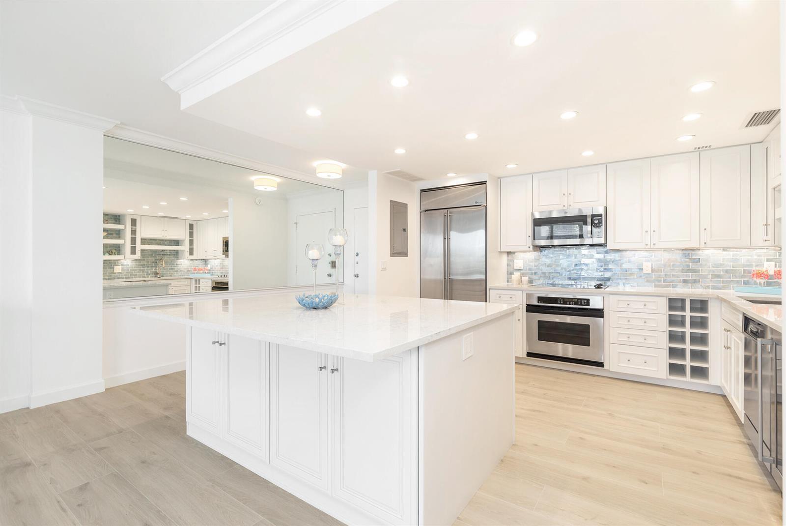 A modern kitchen features white cabinetry, a large marble-topped island, and a blue tiled backsplash — 354 Chilean Avenue # 6c, Palm Beach FL 33480, PALM BEACH, FL