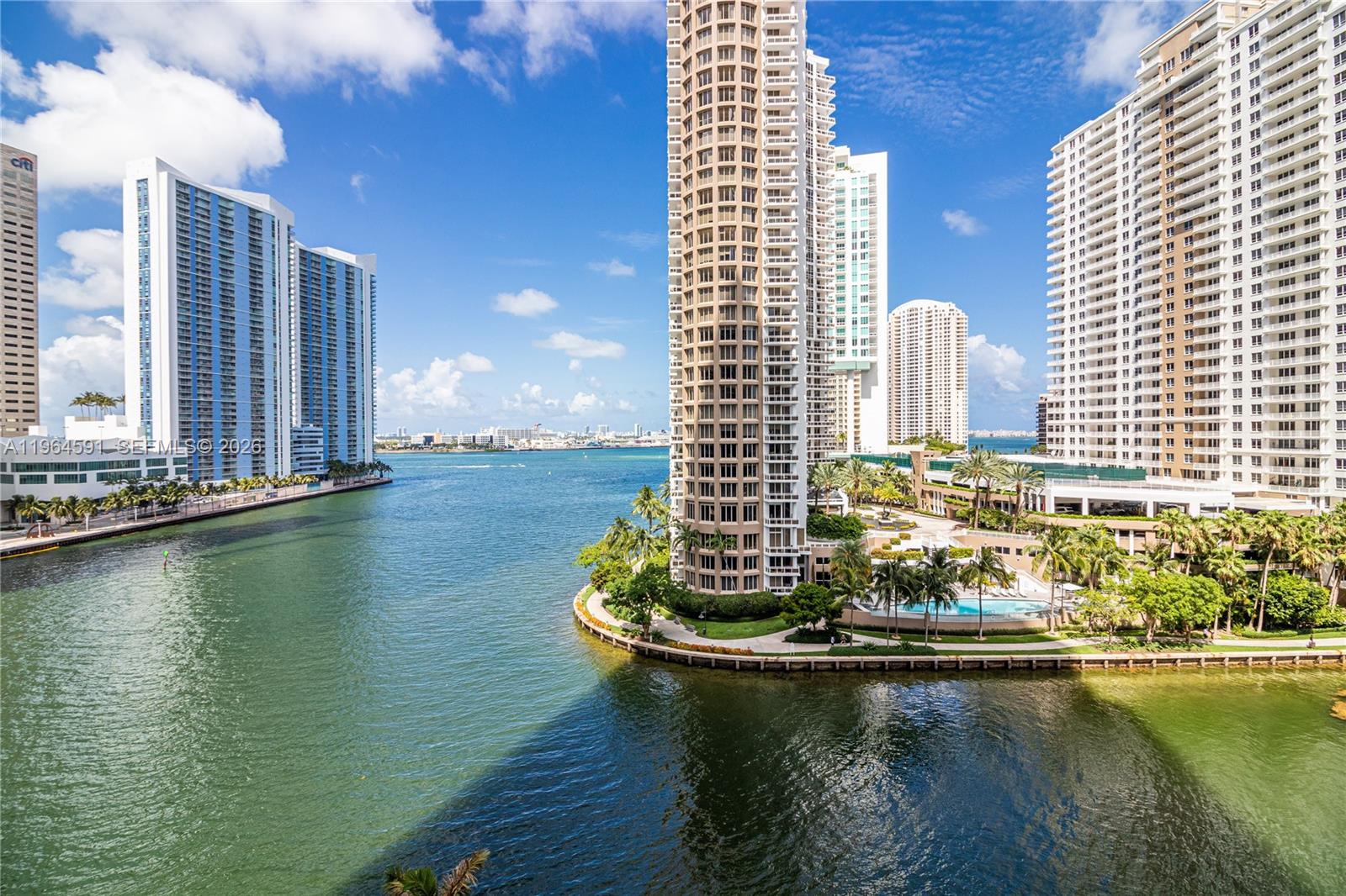 An exterior view shows a waterfront high-rise building surrounded by a pool and palm trees — 465 Brickell Ave # 917, Miami FL 33131, MIAMI, FL