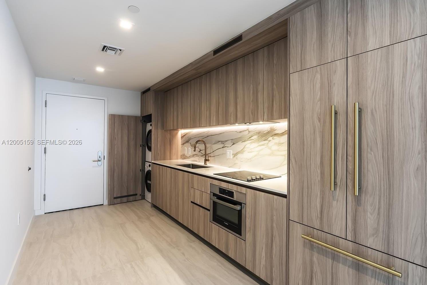 A modern kitchen features wood-grain cabinetry, marble-style backsplash, integrated appliances, and a stacked laundry unit — 77 SE 5th Street # 2515, Miami FL 33131, MIAMI, FL