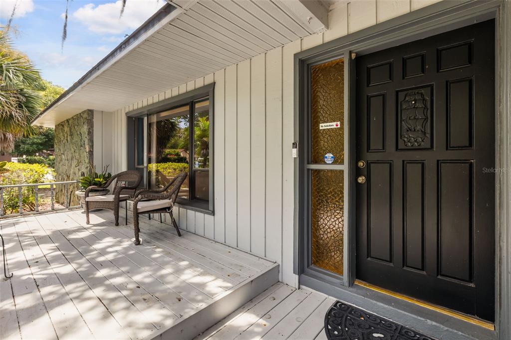 A covered wooden porch features two wicker chairs, a black front door, and vertical siding — 260 QUEENSBERRY COURT, LONGWOOD, FL