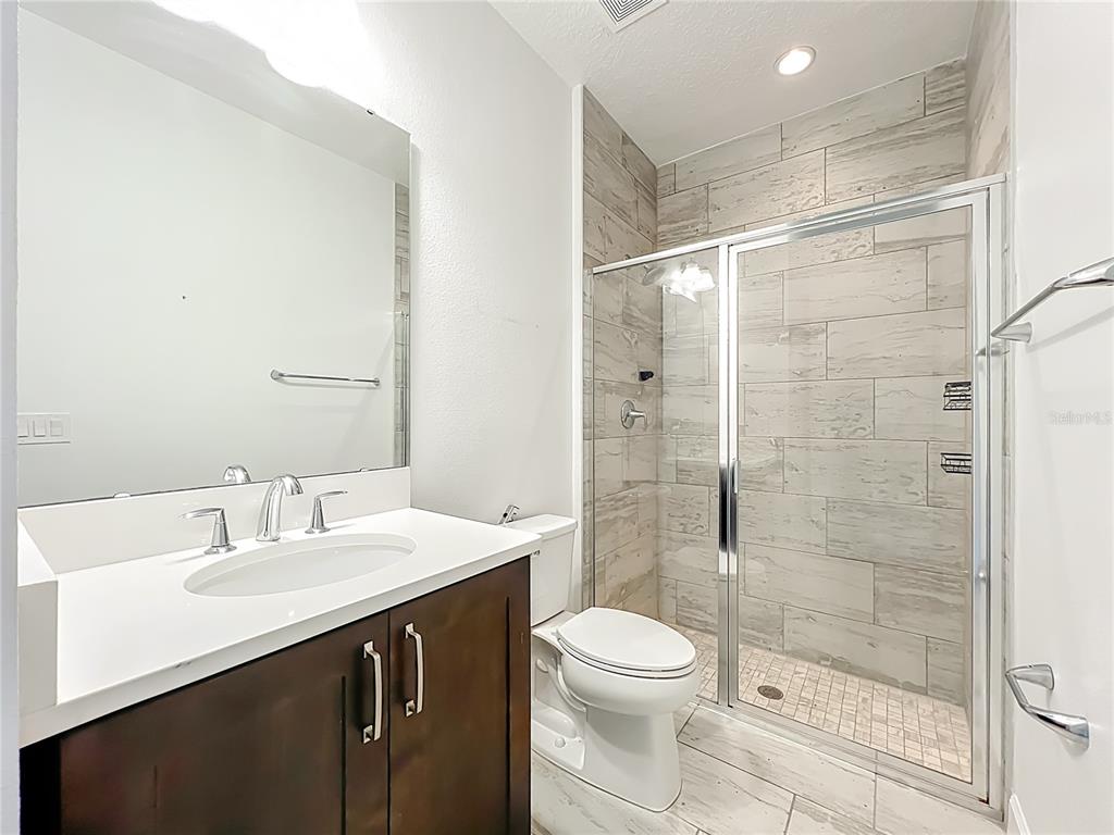 A bathroom features a dark wood vanity, a white countertop, and a glass-enclosed tiled shower — 3392 BLUFF OAK LANE, SANFORD, FL