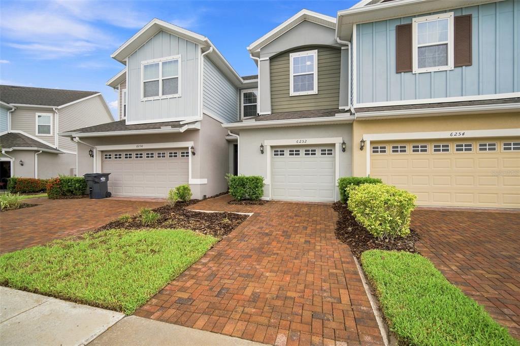 A row of three attached townhouses with brick driveways, green lawns, and multi-colored siding — 6252 CAMINO DRIVE, APOLLO BEACH, FL