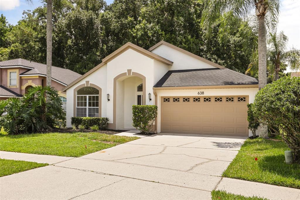 A single-story house with a white stucco exterior, a tan garage door, and a concrete driveway — 638 TALL OAKS TERRACE, LONGWOOD, FL