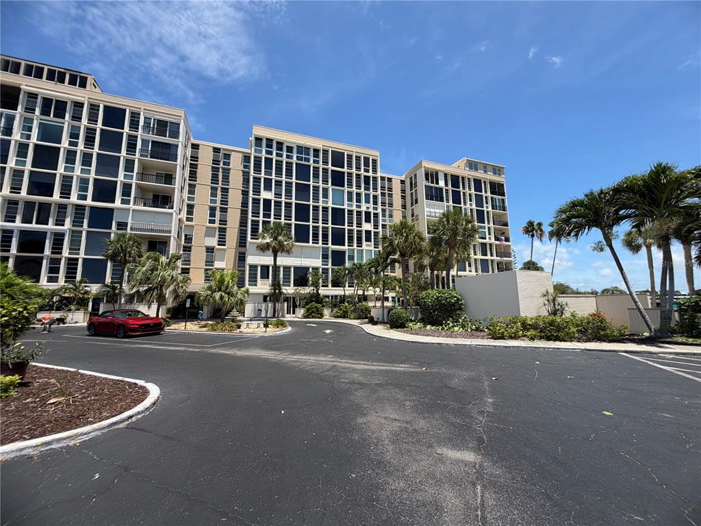 A multi-story apartment building with a parking lot and palm trees under a blue sky — 7400 SUN ISLAND DRIVE S UNIT 111, SOUTH PASADENA, FL