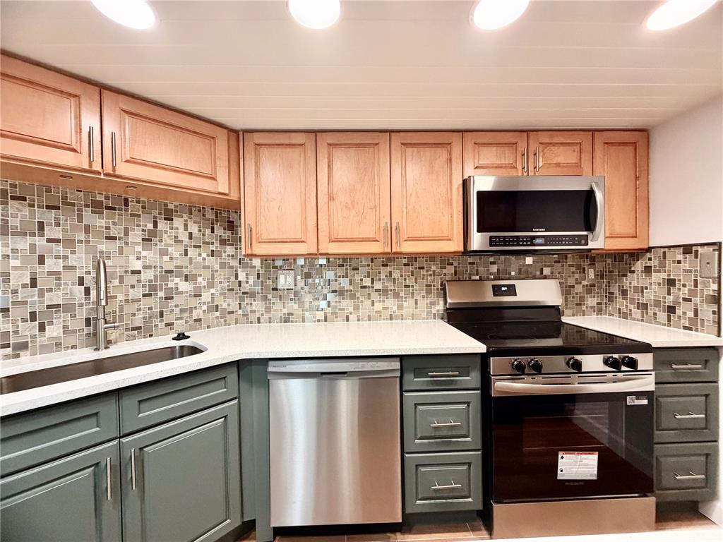 A kitchen features two-toned cabinets, a mosaic tile backsplash, stainless steel appliances, and white countertops — 7400 SUN ISLAND DRIVE S UNIT 111, SOUTH PASADENA, FL