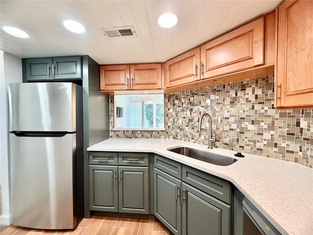 A kitchen features green lower cabinets, wood upper cabinets, a mosaic backsplash, and stainless appliances — 7400 SUN ISLAND DRIVE S UNIT 111, SOUTH PASADENA, FL