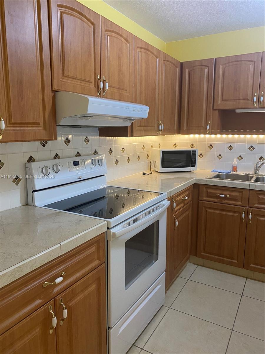 A kitchen features wood cabinets, white appliances, a tiled backsplash, and light-colored countertops — 9301 SW 92nd Ave # 210C, Miami FL 33176, MIAMI, FL