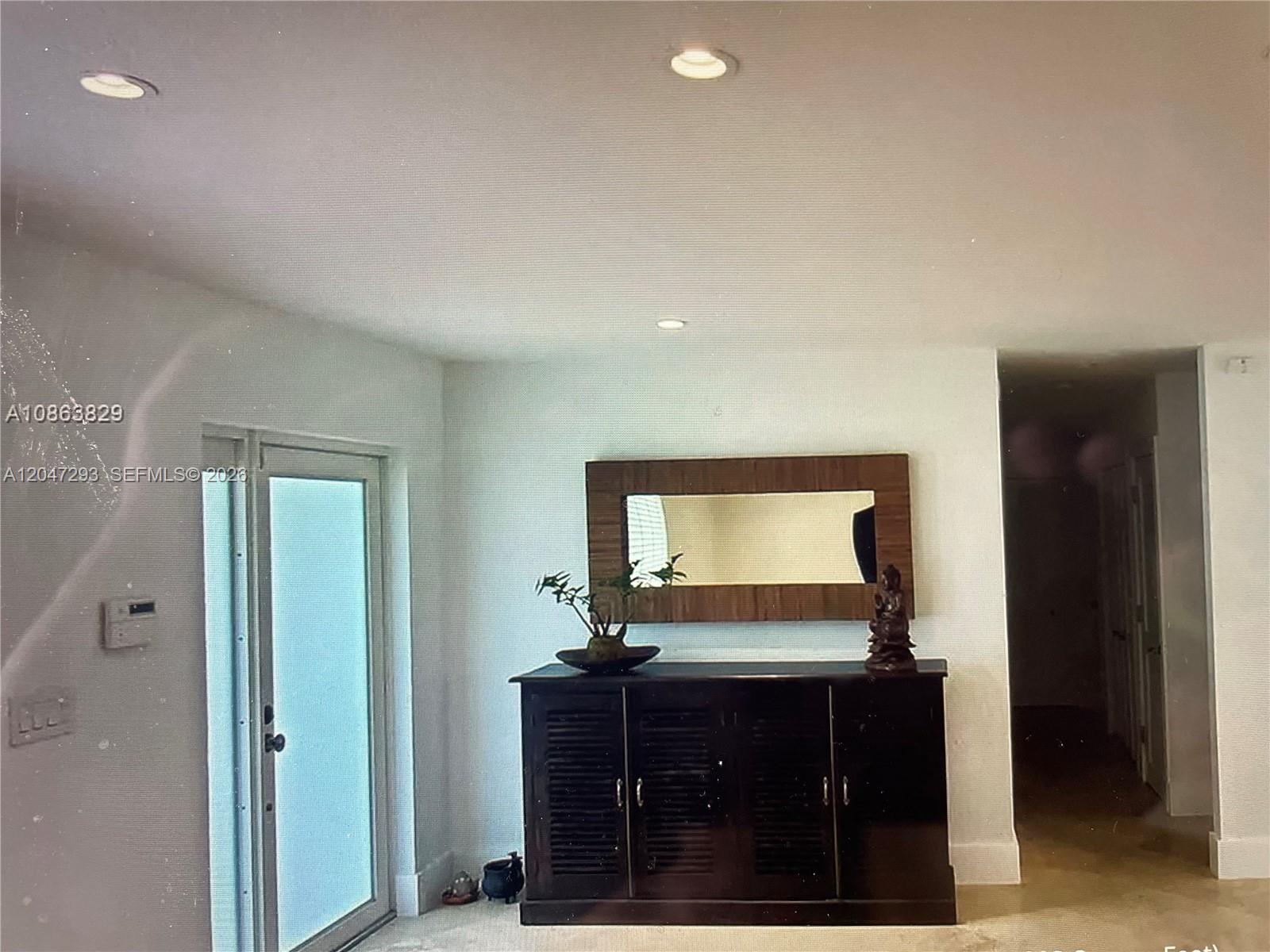 A dark wood cabinet with a mirror sits against a white wall near a doorway — 10900 SW 107th Ave, Miami FL 33176, MIAMI, FL