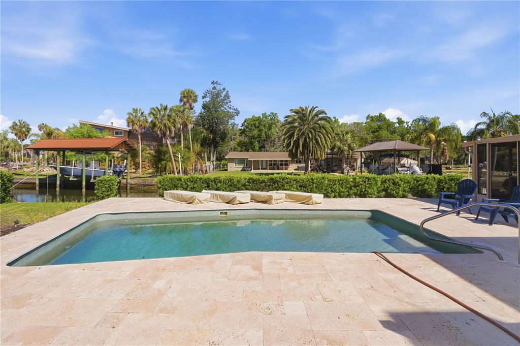 A swimming pool with a stone deck overlooks a canal with boat docks and palm trees — 9235 W HARBOR ISLE COURT, CRYSTAL RIVER, FL