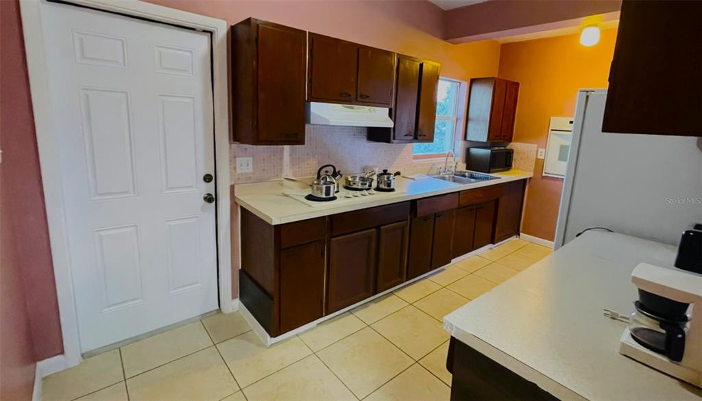 A kitchen features dark wood cabinets, light countertops, a white door, and tiled flooring — 554 LINDLEY TERRACE, PORT CHARLOTTE, FL