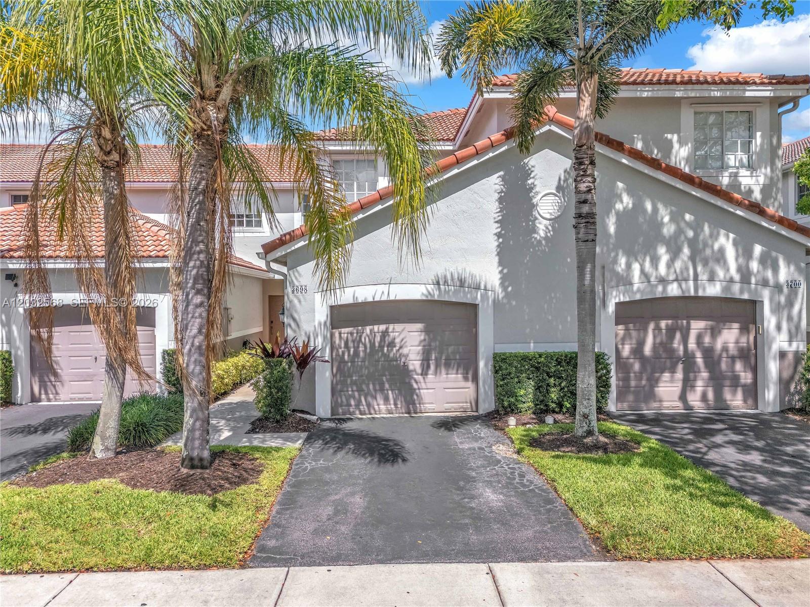 A two-story townhouse exterior features a beige stucco facade, tile roof, and two garage doors — 3698 San Simeon Cir, Weston FL 33331, WESTON, FL