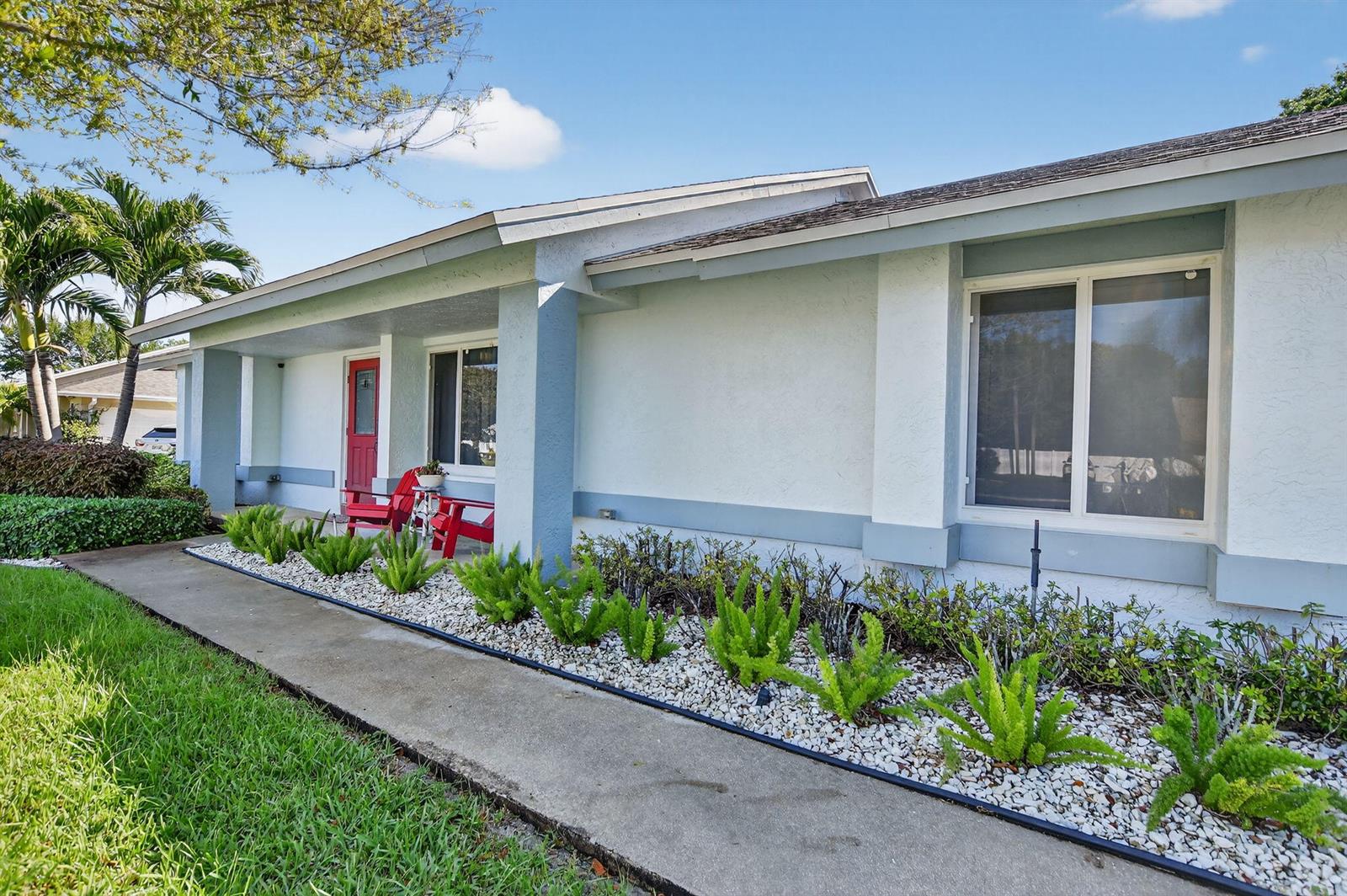 A light-colored house exterior features a concrete walkway, white rock landscaping, and red chairs — 18298 102nd Way, Boca Raton FL 33498, BOCA RATON, FL