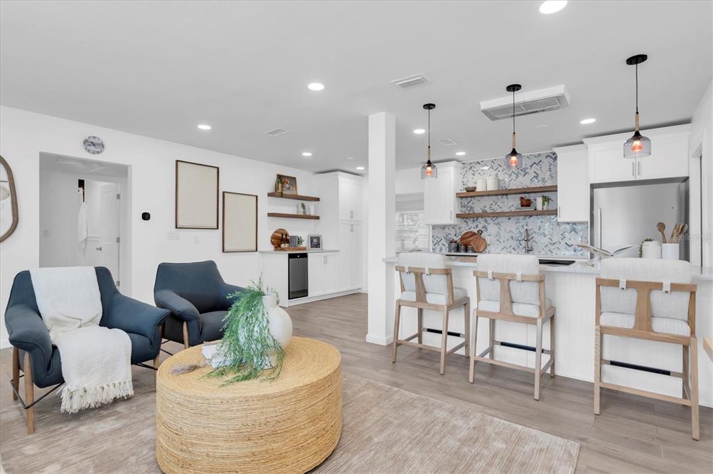 A bright, open-concept kitchen and living area featuring white cabinetry, blue chairs, and bar seating — 197 LIDO DRIVE, ST PETE BEACH, FL