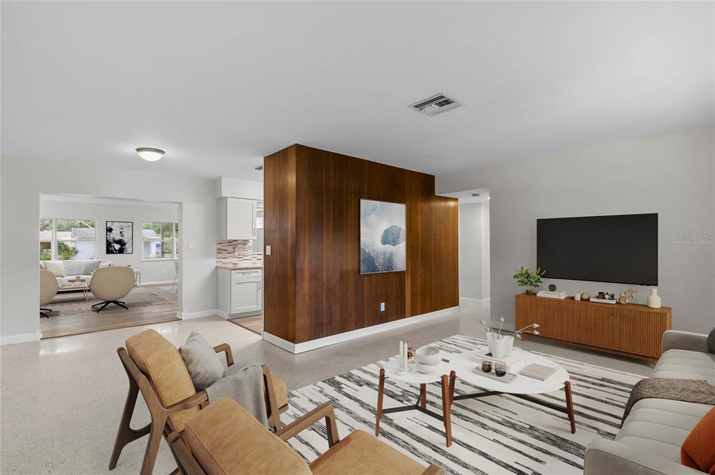A living room features a wood-paneled accent wall, terrazzo floors, and a view into a kitchen — 2910 W PRICE AVENUE, TAMPA, FL