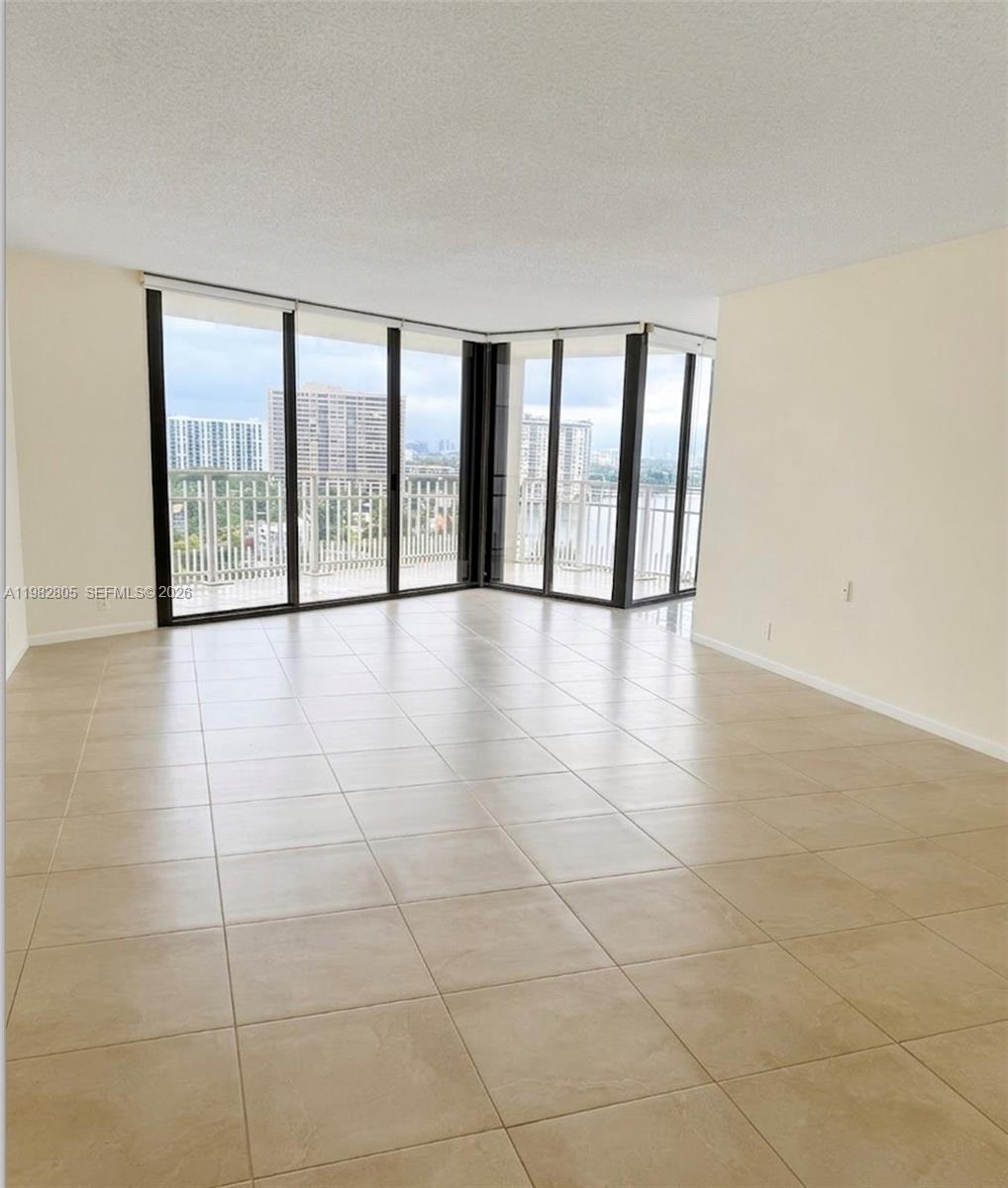 An empty room with beige tile flooring and floor-to-ceiling windows overlooking a city skyline — 4000 Towerside Ter # 1401, Miami FL 33138, MIAMI, FL