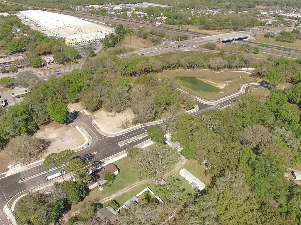 An aerial view shows a newly paved road intersection, a retention pond, and surrounding wooded areas — 6011 COUNTY ROAD 579, SEFFNER, FL