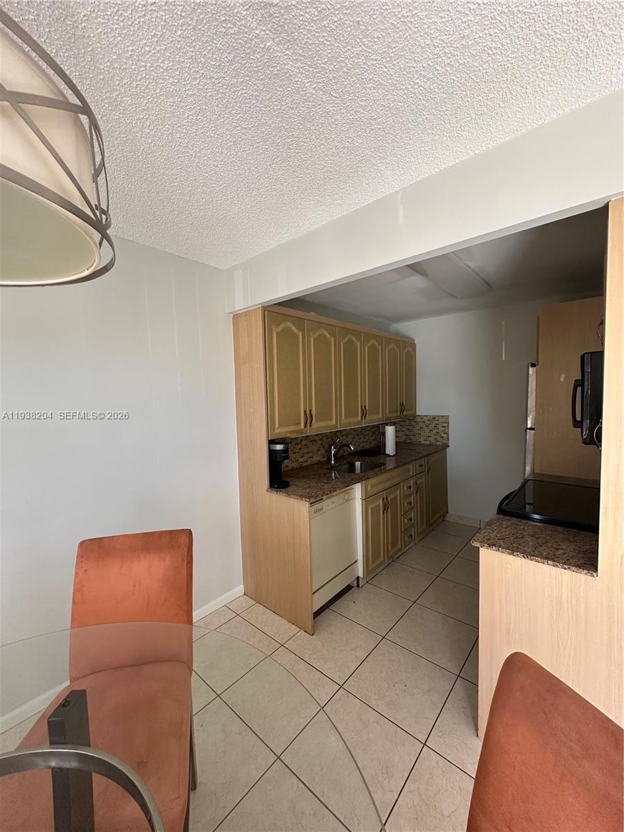 A small kitchen features light wood cabinets, granite countertops, and beige tile flooring — 3043 Exeter, Boca Raton FL 33434, BOCA RATON, FL