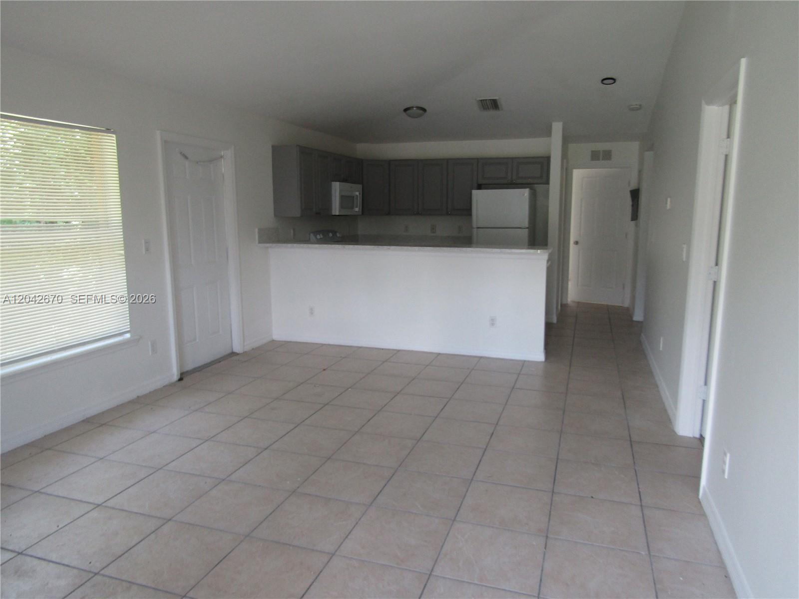 An open-concept kitchen with grey cabinets and a white breakfast bar overlooks a tiled room — 625 Meadow # 625, Lehigh Acres FL 33973, LEHIGH ACRES, FL