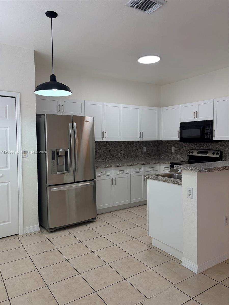 A kitchen features white cabinets, stainless steel appliances, granite countertops, and light-colored tile flooring — 12393 SW 124th Ter, Miami FL 33186, MIAMI, FL
