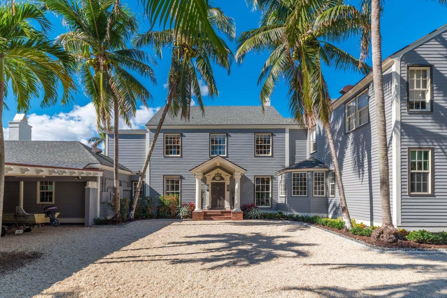 A two-story gray house with a gravel driveway and palm trees under a blue sky — 15 S Lake Trail, Palm Beach FL 33480, PALM BEACH, FL