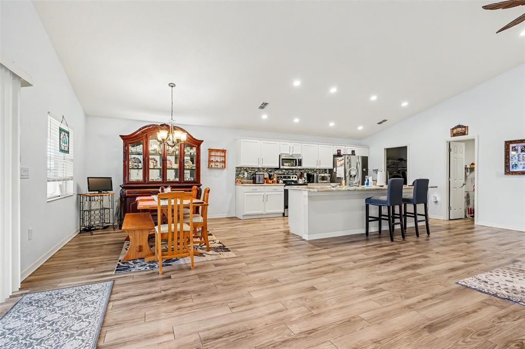 A kitchen with a white island and light wood flooring opens into a large living area — 3913 WHITE IBIS RD, LAKELAND, FL