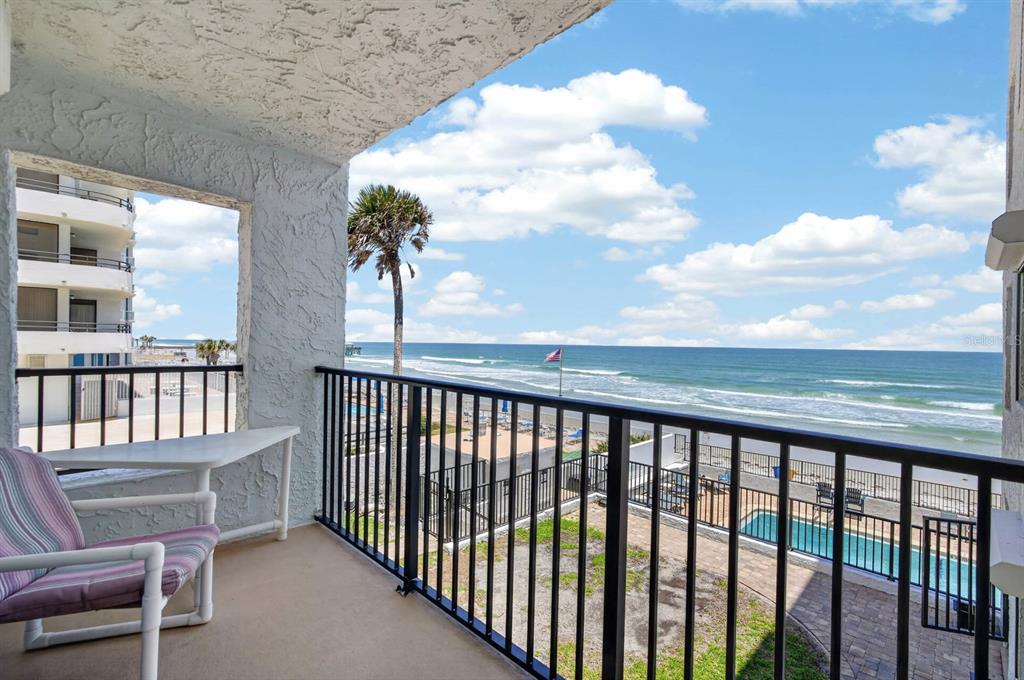 A balcony with a white chair overlooks a swimming pool, beach, and the ocean — 3747 S ATLANTIC AVENUE UNIT 2020, DAYTONA BEACH, FL