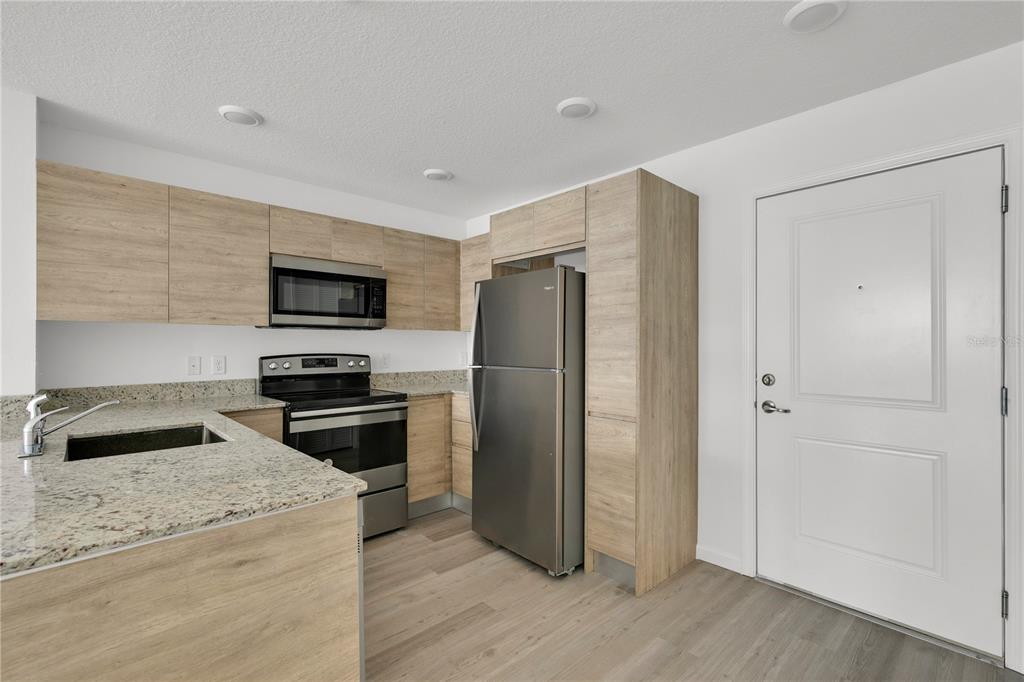 A kitchen features light wood cabinets, granite countertops, stainless steel appliances, and a white door — 1230 SOUTHSTATION PLACE UNIT 105, ORLANDO, FL