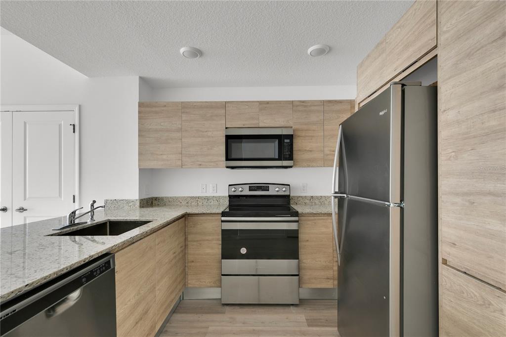 A kitchen featuring light wood cabinets, stainless steel appliances, and granite countertops — 1230 SOUTHSTATION PLACE UNIT 105, ORLANDO, FL