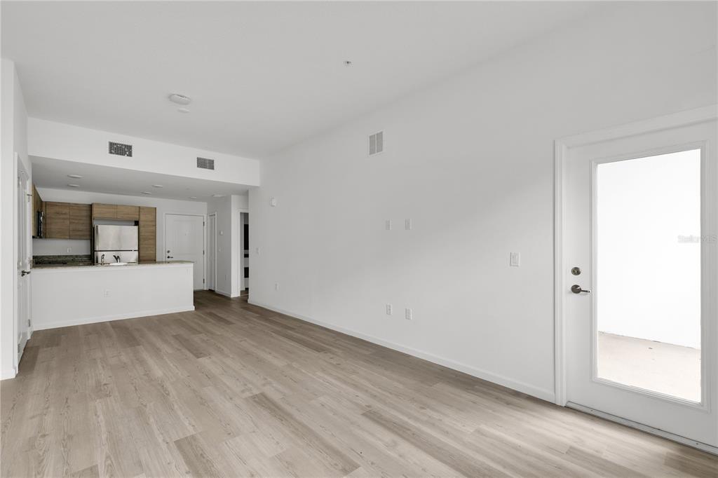 An open-concept living area features light wood-look flooring, white walls, and an adjacent kitchen — 1230 SOUTHSTATION PLACE UNIT 105, ORLANDO, FL