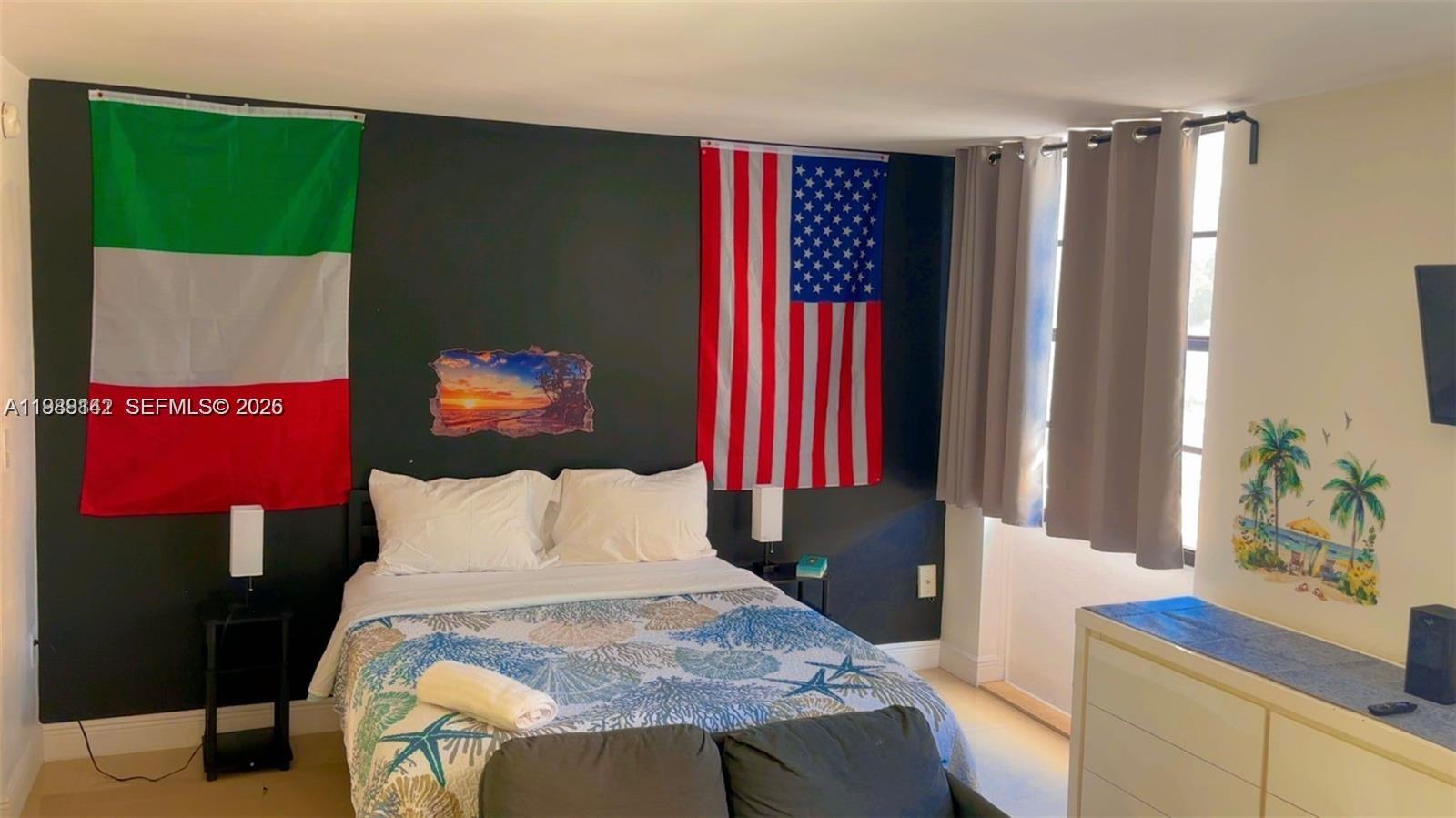 A bedroom features a bed with a patterned quilt, two wall flags, and dark accent walls — 710 Washington Ave # 209, Miami Beach FL 33139, MIAMI BEACH, FL