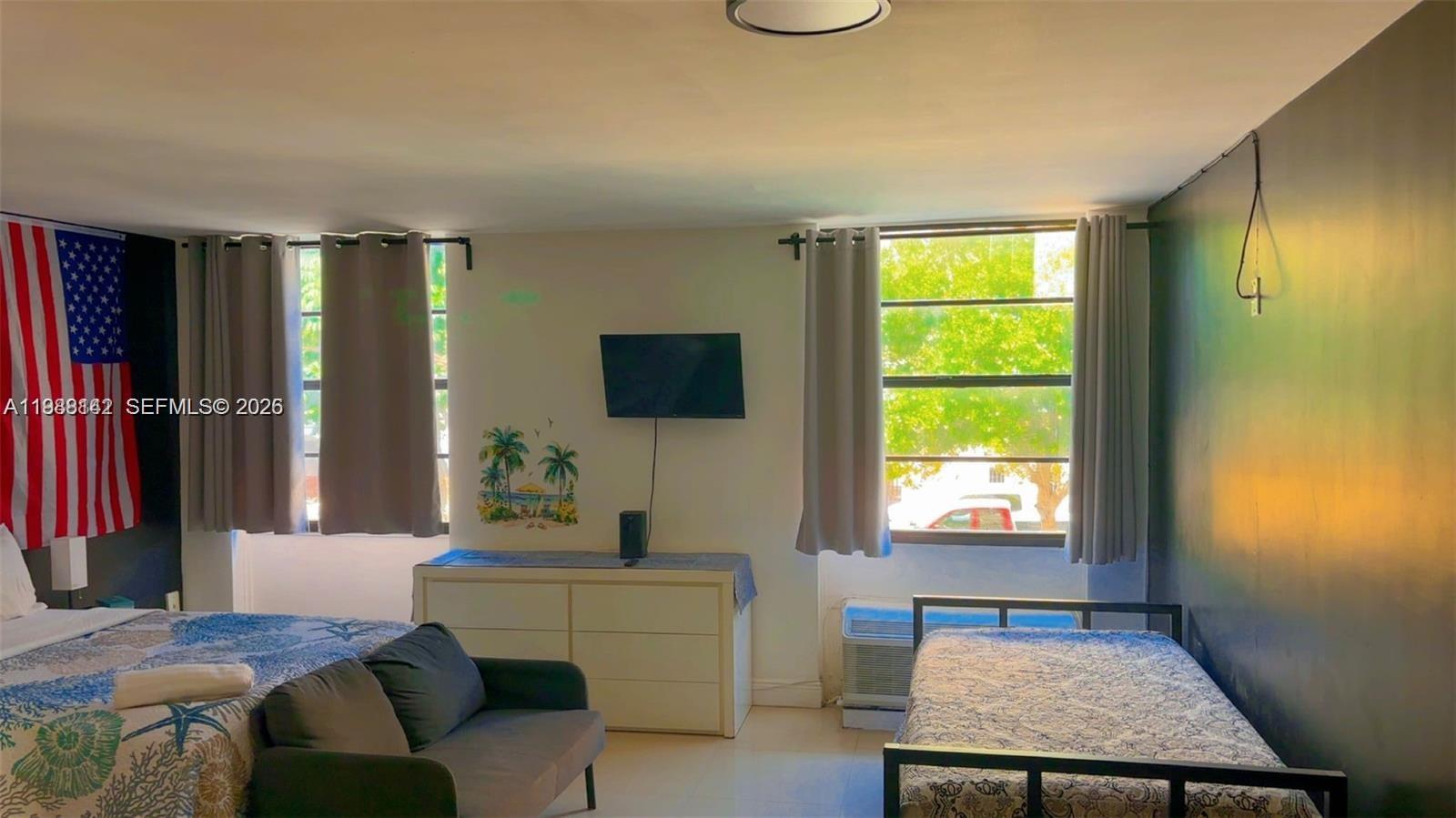 A bedroom features two beds, a small sofa, a dresser, and a wall-mounted television — 710 Washington Ave # 209, Miami Beach FL 33139, MIAMI BEACH, FL