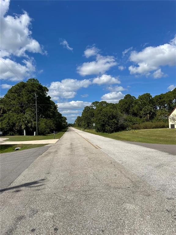 A paved road stretches into the distance between grassy shoulders and dense green trees — 12325 CHAMBERLAIN BOULEVARD, PORT CHARLOTTE, FL