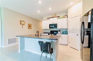 A kitchen features white cabinets, a granite island with a chair, and stainless steel appliances — 5722 KEATON SPRINGS DRIVE, LAKELAND, FL