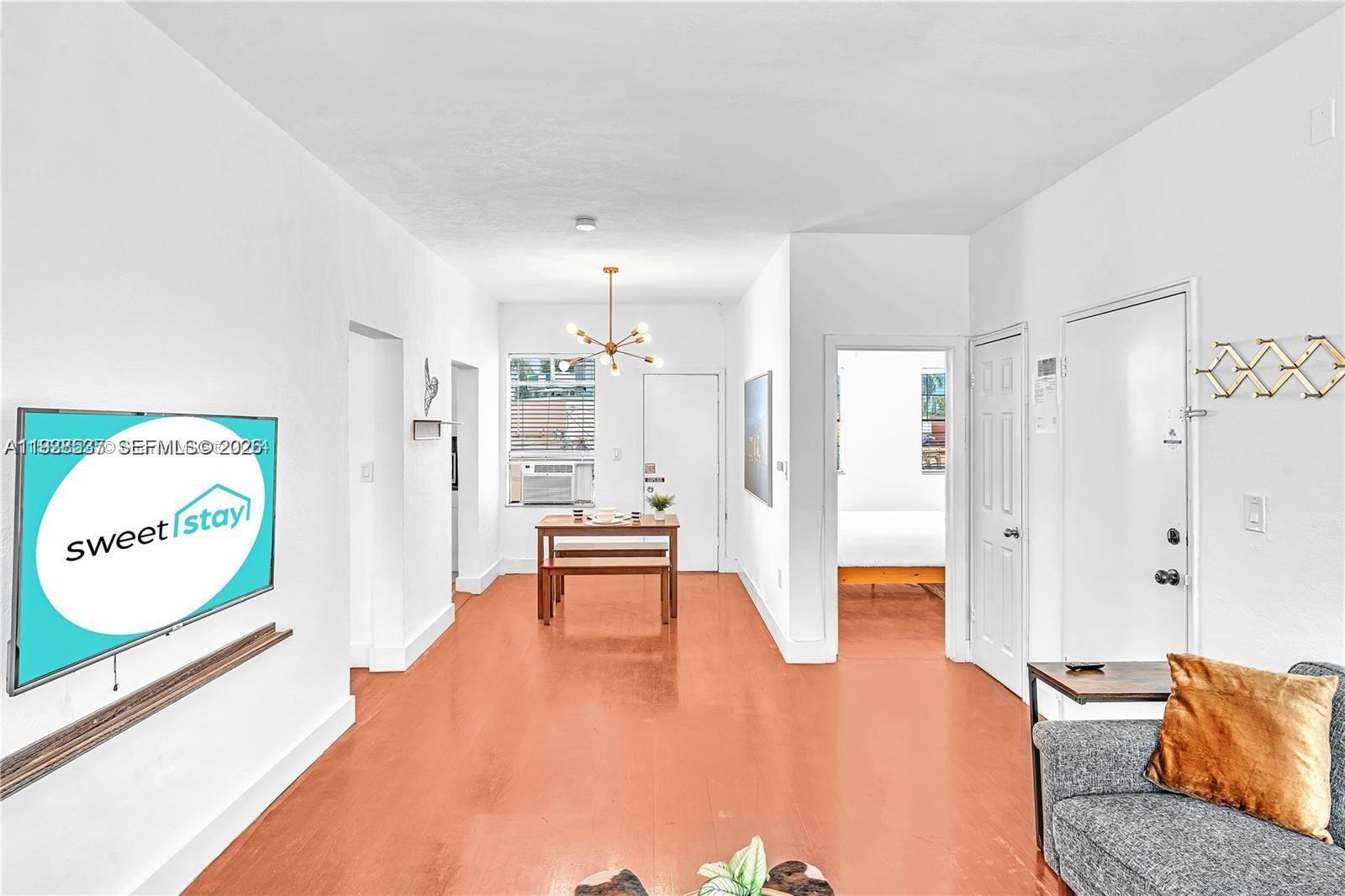 This living area features light wood-look flooring, a dining set, and a wall-mounted television — 3920 Garden Ave # 14, Miami Beach FL 33140, MIAMI BEACH, FL