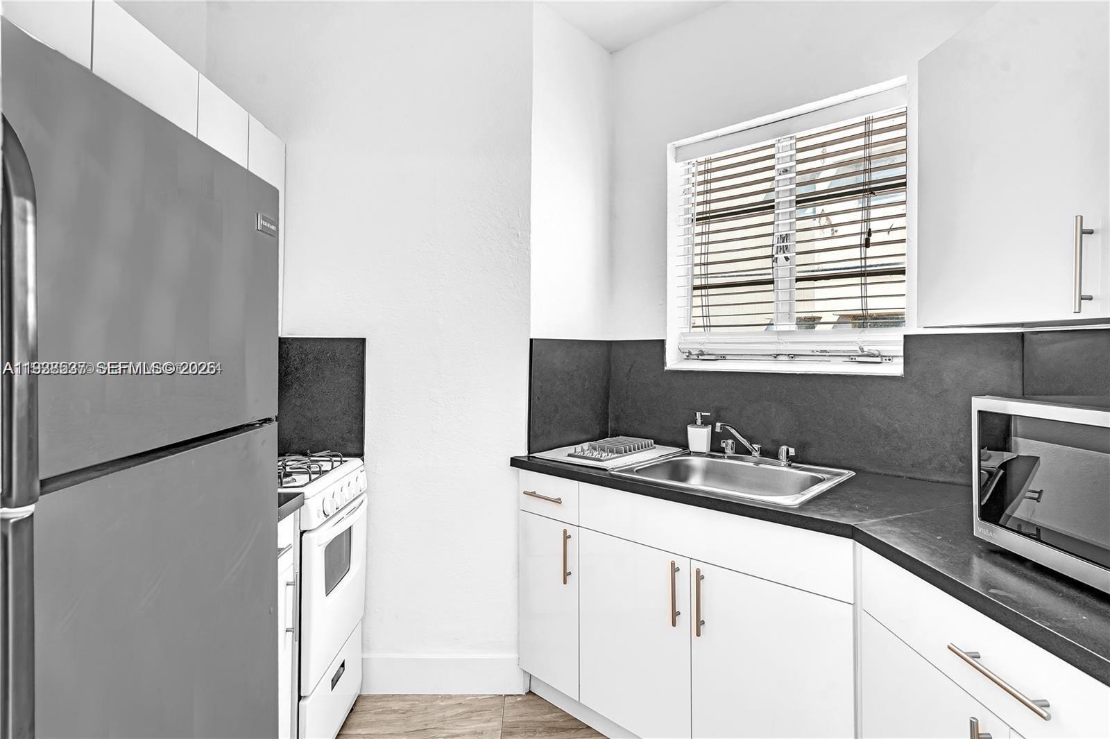 A kitchen features white cabinets, black countertops, a stainless steel refrigerator, and a white stove — 3920 Garden Ave # 14, Miami Beach FL 33140, MIAMI BEACH, FL