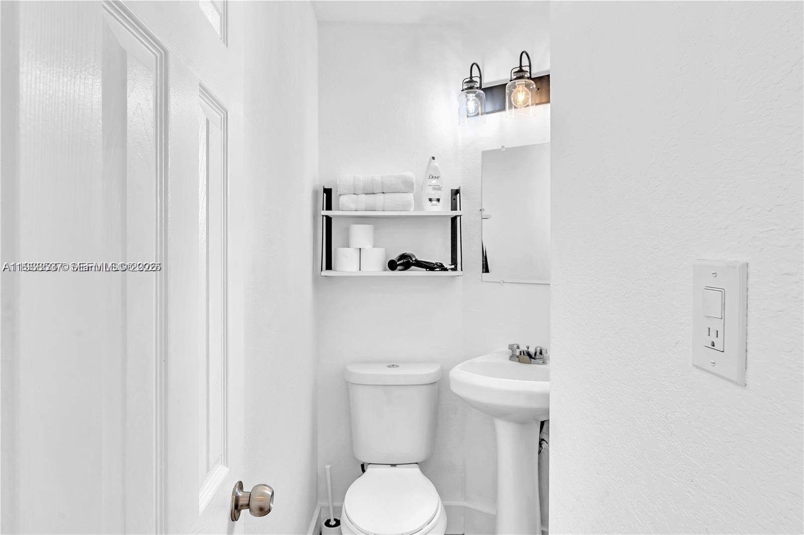 A small bathroom features a white pedestal sink, a toilet, and wall-mounted shelving — 3920 Garden Ave # 14, Miami Beach FL 33140, MIAMI BEACH, FL